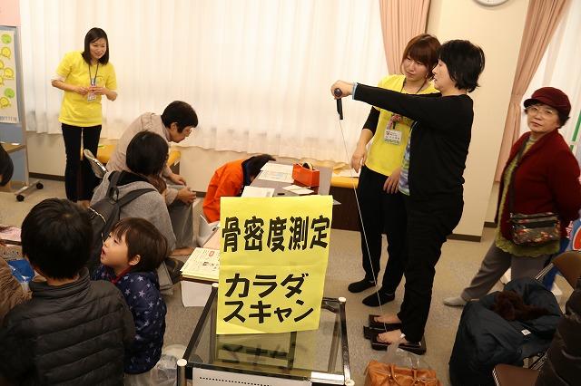 体重計に乗ってレバーを持った両腕を前に伸ばし、骨密度を測定しているイベントの写真