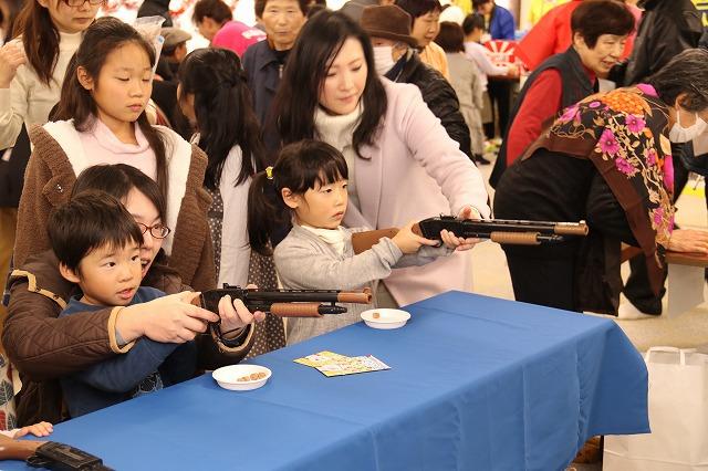 射的で真剣な目で景品を狙っている子どもと後ろからフォローしている親の写真