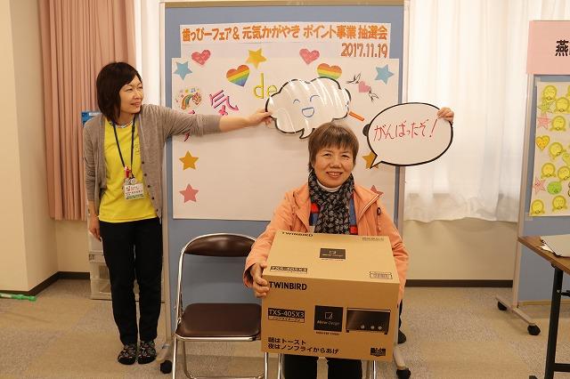 当選したトースターを抱えて椅子に座っている女性の写真