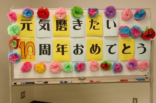 紙の花で飾られている「元気磨きたい10周年おめでとう」と書かれたホワイトボードの写真