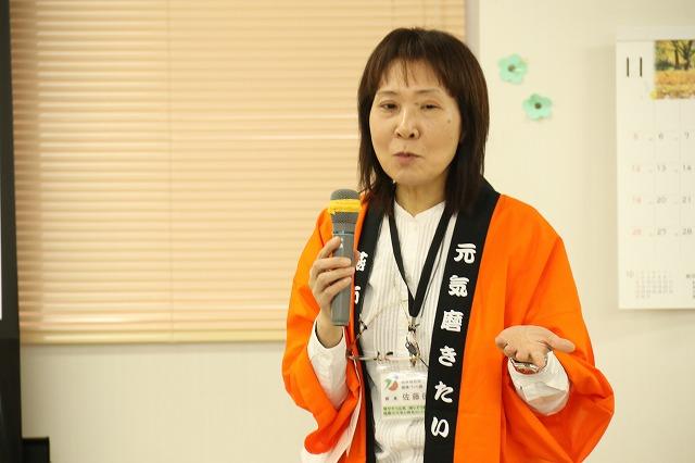 オレンジのハッピを着てマイクを手に話している女性の写真