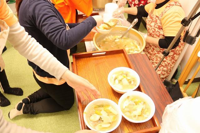 大きな鍋から豚汁を器によそう人と、手前に置かれたお盆に乗せている様子の写真