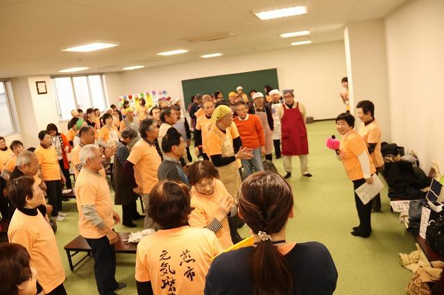 参加者たちが一同に集ってマイクを手に離している女性の話を聞いている写真