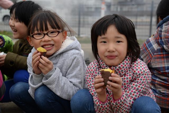 真ん中で割った焼き芋を手にして喜んでいる2人の子どもの写真