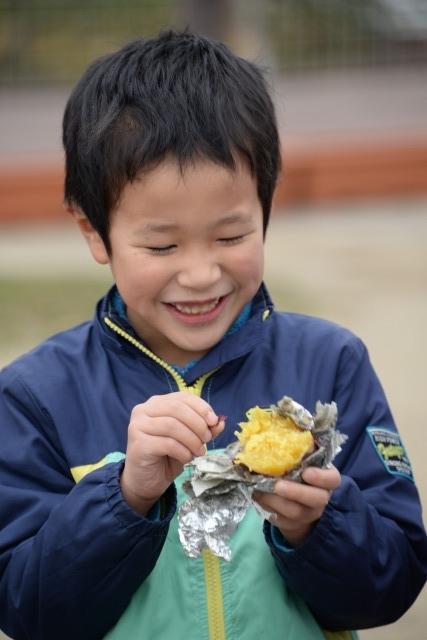 アルミホイルに包まれた黄色い断面の焼きいもを手に持って、満面の笑みの少年の写真
