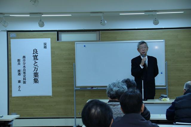 二人がけの机に並んで座っている参加者たちのと、前に立って話をしている白髪混ざりの男性の写真