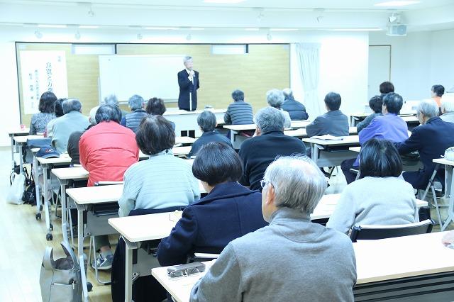 「親子版画づくり講習会」と書かれた垂れ幕がある部屋で、グループに別れて机を囲んで作業をしている参加者の写真