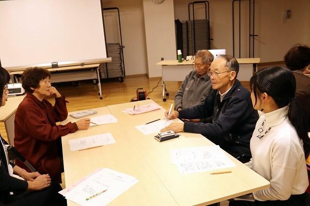 ストレス机を囲んで筆記具を持ち、座って話をしている5人の人々の写真コントロール