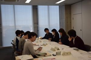 縦に長い机の周りに座り資料を見ながら会議に参加する女性たちの写真