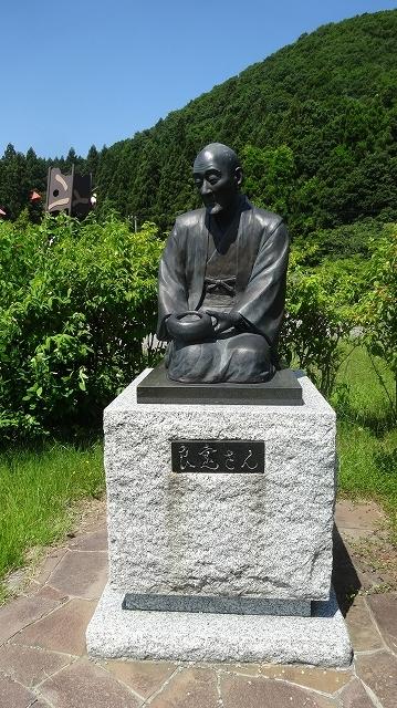 青い空と深い緑の山々を背景に写っている良寛の銅像の写真