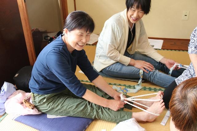 足の指に紐を通して布ぞうりを作ろうとして笑っている女性の様子の写真