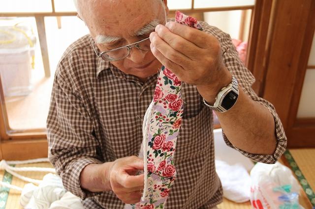 鼻緒用の紐に赤い花の模様の布を巻き付けている男性の写真