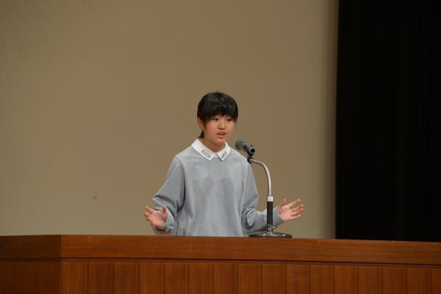 壇上で両手を広げながらスピーチをしている女子の写真
