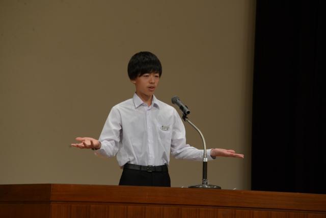 壇上で両手を広げながらスピーチをしている制服姿の男子の様子の写真