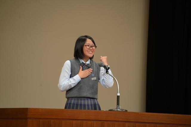 右手を胸に当てて左手でガッツポーズをしながらスピーチをしている制服姿の女子の写真