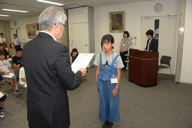 スーツ姿の男性から任命書を受け取ろうとしている女の子の様子の写真