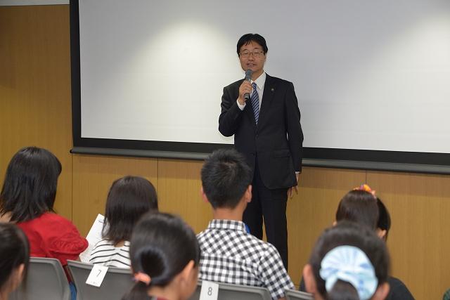 スーツ姿でマイクを持った市長が小学生たちに話をしている様子の写真