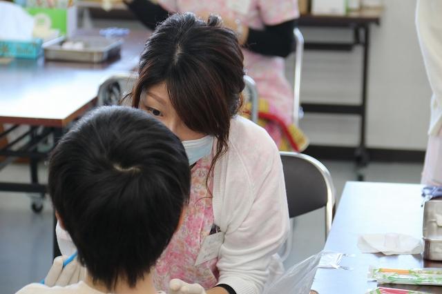パイプ椅子に腰かけ歯科検診をするマスクを装着した女性と検診を受ける男の子の写真