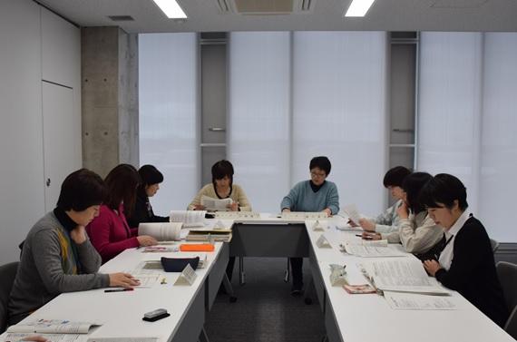 コの字に置かれた椅子に座り机の上の資料を眺めながら会議に参加する女性たちの写真