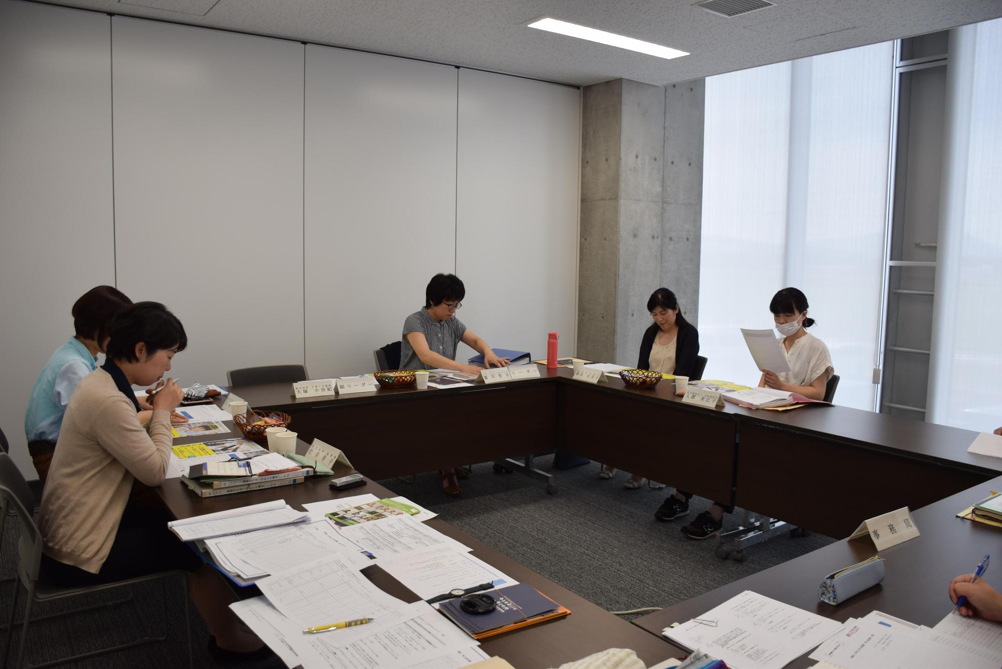 四角く並べられた机の周りに座り資料を見ながら会議に参加する女性たちの写真
