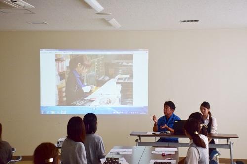 参加者の前で壁のスクリーンに映像を映して説明をしている写真