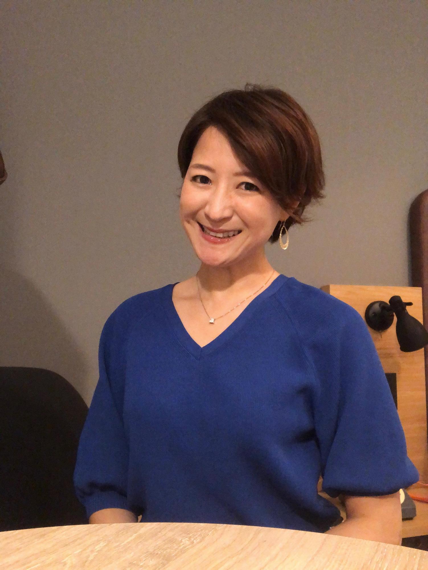 青い半袖の服を着て写真に笑顔でこたえる女性の写真