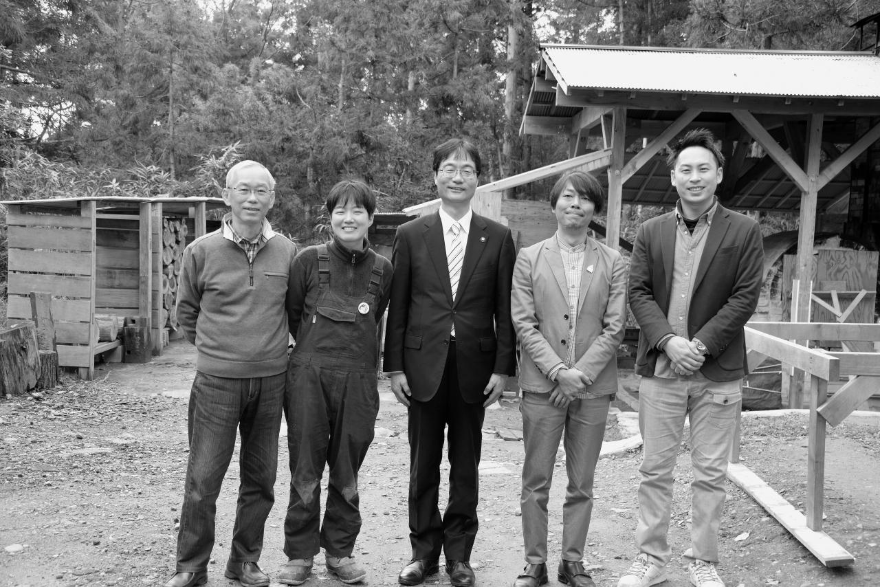 木々に囲まれた工房の外で記念撮影する参加者たちの写真