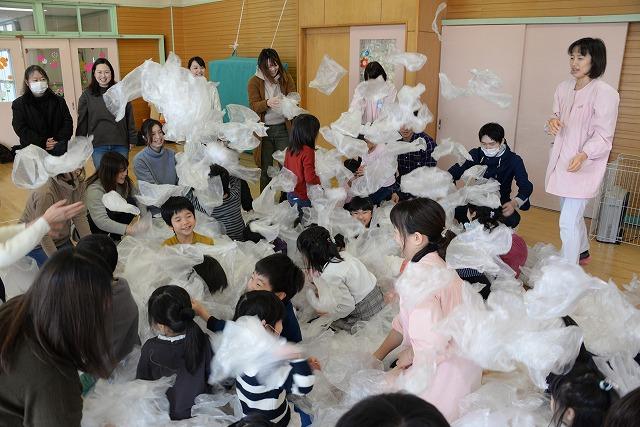 保育園の遊戯室にて音楽に合わせて大量のビニール袋と戯れている子どもたちの写真