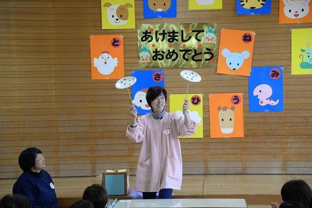ステージ上で両手に棒を持ち皿回しを披露する女性保育士の写真