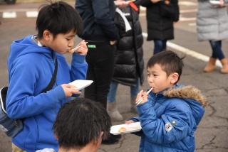 つきたて餅で作ったきな粉餅を橋を使って食べている2人の子どもたちの写真
