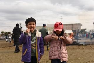 塞の神の火であぶったスルメを食べる2人の子どもの写真