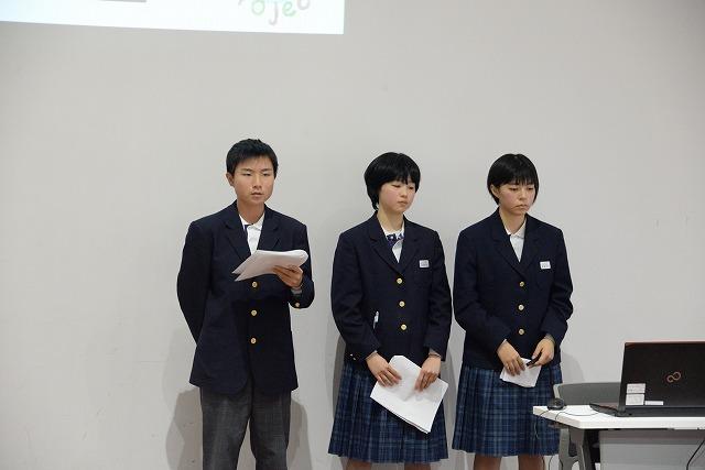 パソコンが置かれた長机の横に立ち、書類を手にしている3人の学生達