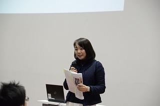 書類とマイクを手に、話をしている女性の写真