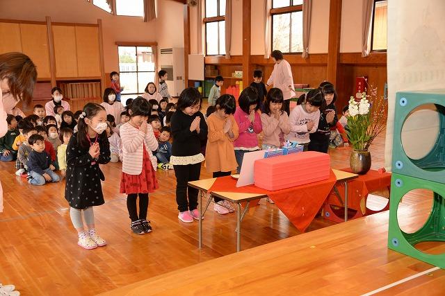 前に置かれた長机の前に横並びに立ち、その奥にある掛け軸に向かって手を合わせている9人の女の子達の写真