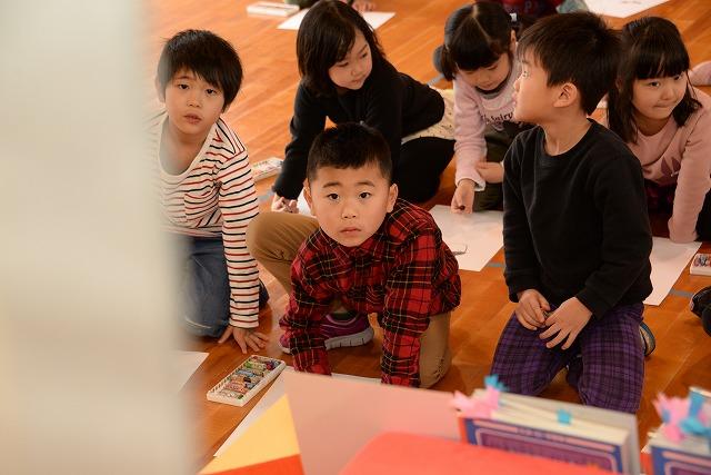 クレヨンを手に、座りながら掛け軸をじっと見つめて何かを描いている男の子の写真
