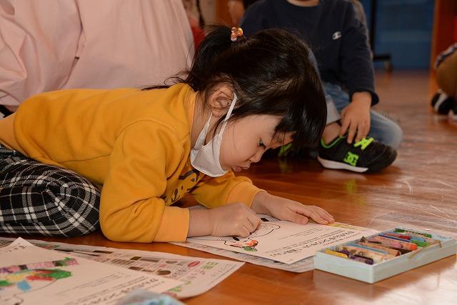 床に塗り絵の紙を置き、クレヨンで塗り絵に集中している女の子の写真