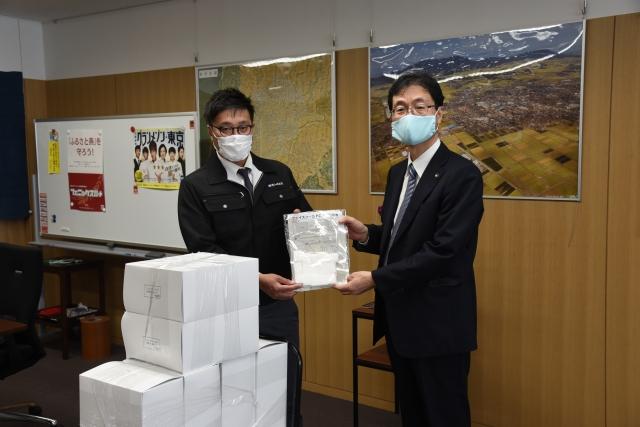 スーツ姿の市長が会議室内で箱に入ったフェイスシールドを受け取っている写真
