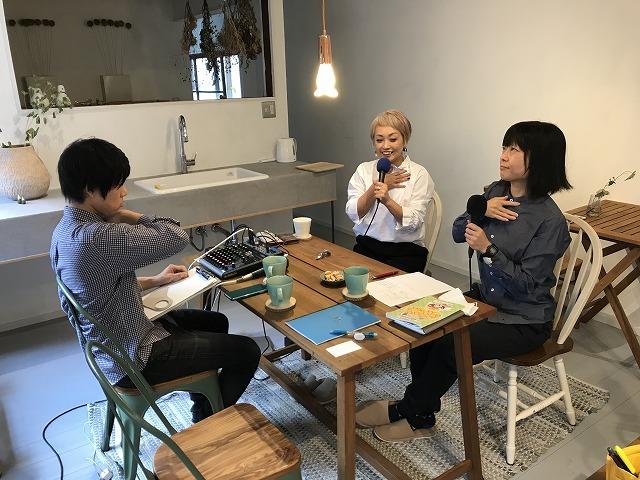 椅子に座った女性2名と男性1名とが、椅子に鎖骨のあたりに手を当てるしぐさをしている写真