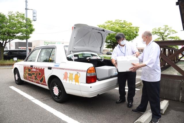発泡スチロールの箱を手渡している男性と、タクシーのトランクを開けて受け取っている運転手の写真
