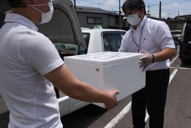 白い箱を手渡している運転手の男性と、受け取っている男性の写真