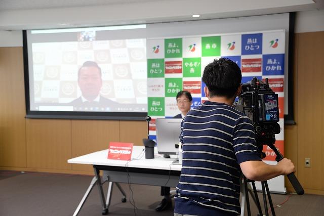 男性の写っているスクリーンの隣で、パソコンを前に話している市長と、その様子を撮影しているカメラマンの写真