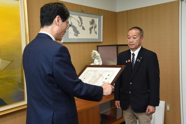 感謝状を読み上げている男性と、向かい合って聞いているジャケットを着た男性の写真