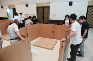 屋内で段ボール製のパーティションを組み立てている職員たちの写真