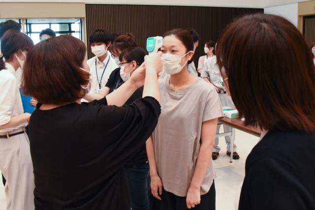 ハンドタイプの非接触型体温計を額にかざされ体温を測られている女性職員の写真