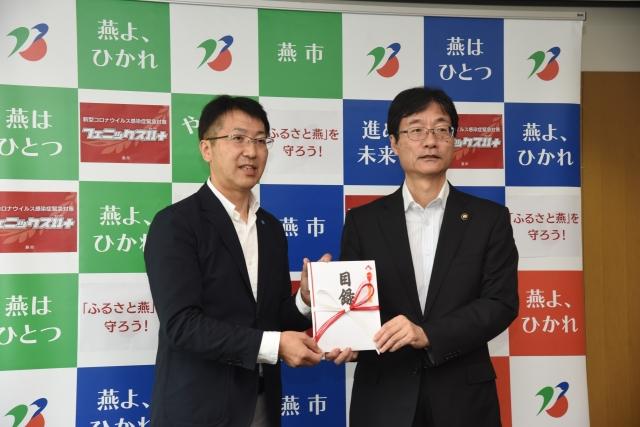 目録を共に手に取り掲げながら並ぶ2人のスーツ姿の男性の写真