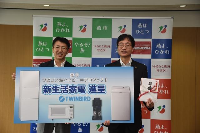 目録とつばコンdeハッピー∞プロジェクトのポップを掲げながら並ぶ2人のスーツ姿の男性の写真