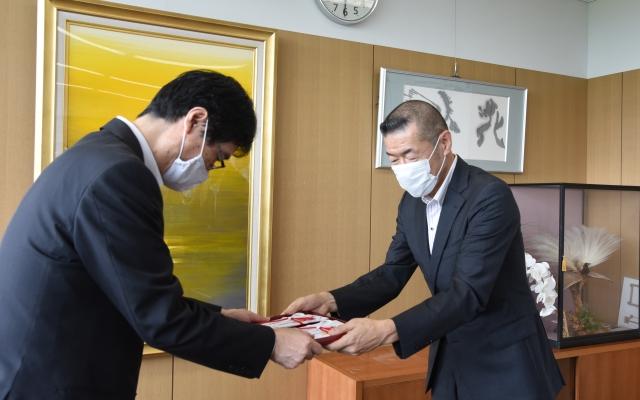 スーツ姿にマスクを付けた男性が寄付金の入ったのし袋を、同じくスーツ姿にマスクを付けた男性職員へと渡している写真