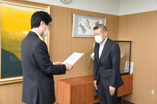 スーツ姿にマスクを付けた男性職員が、同じくスーツ姿にマスクを付けた男性へお礼状の受け渡しを行っている写真