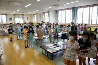 窓から光差し込む明るい広い教室の中で立って整列している男女の子供たちの写真