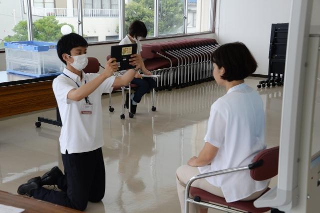 椅子に座っている女性の顔写真をタブレットを使って撮影している職員の写真